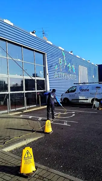 Terry, iShine’s owner/operator, cleaning the cladding and glazing of a commercial building, with the iShine van parked beside it