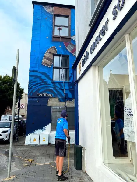 Terry, iShine’s owner/operator, cleaning the windows of a mural-painted building in town