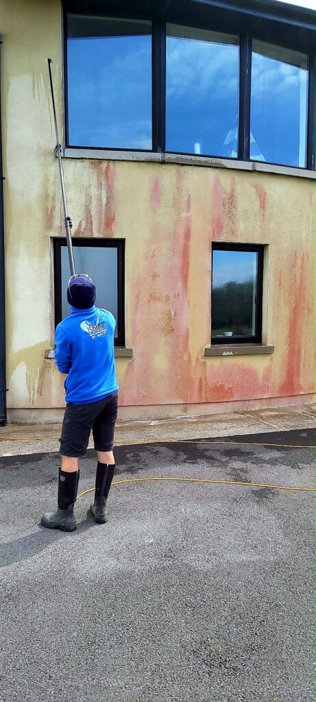 Terry, iShine’s owner/operator, washing red algae off a rendered wall with a water-fed pole