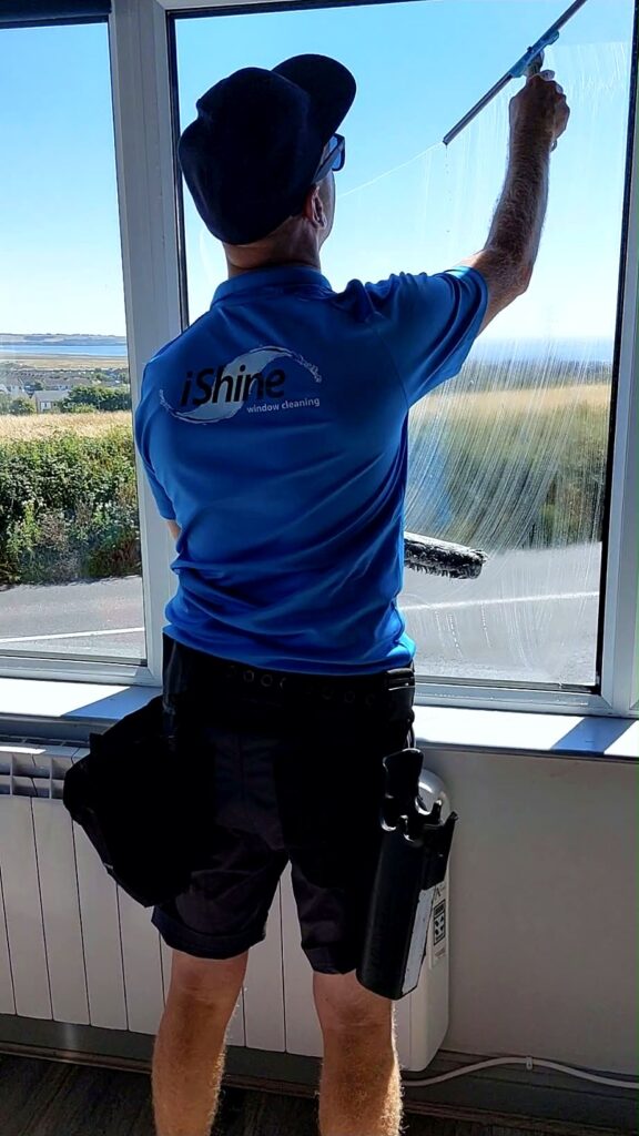 Terry, iShine’s owner/operator, cleaning a large window with a squeegee
